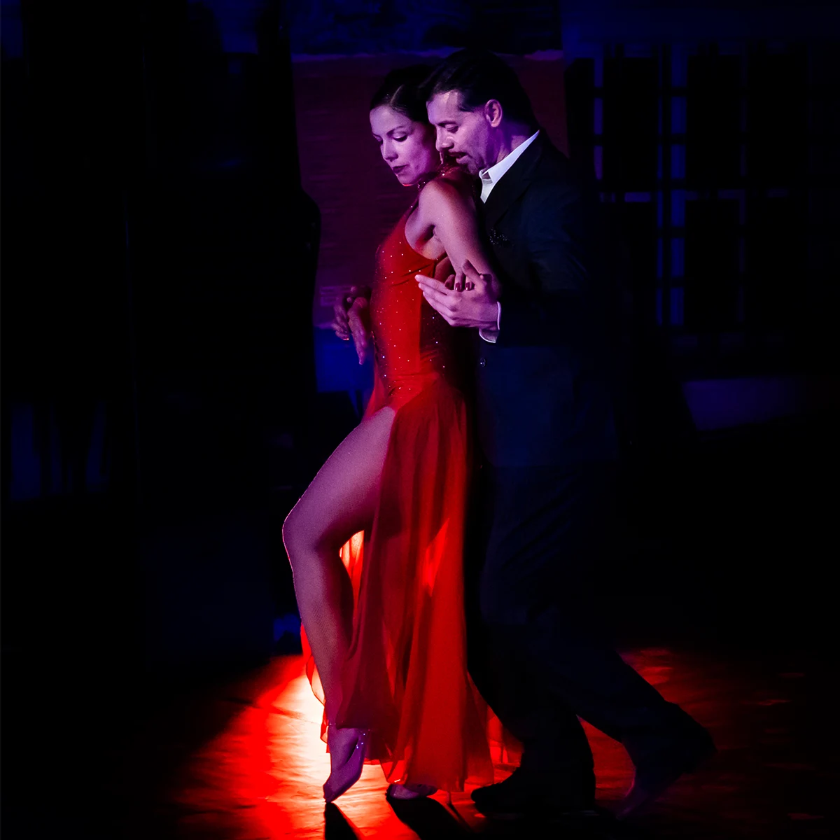 Coppia di ballerini di tango in abito rosso in un passo di danza sotto una luce radente sul palco