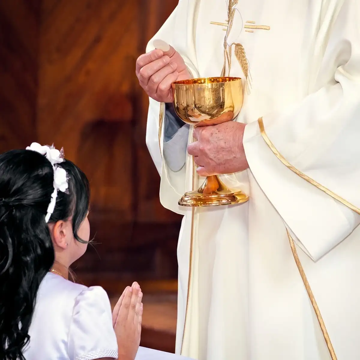 Fotografo per cresime a Genova: bambina in preghiera davanti al sacerdote durante il sacramento in chiesa