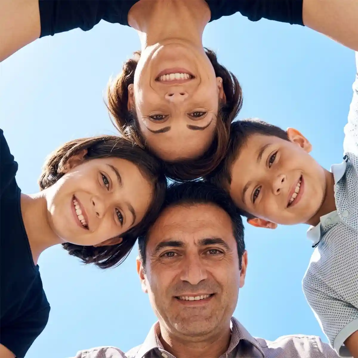 Ritratto di famiglia: padre, madre e due figli in cerchio ripresi dal basso contro il cielo azzurro