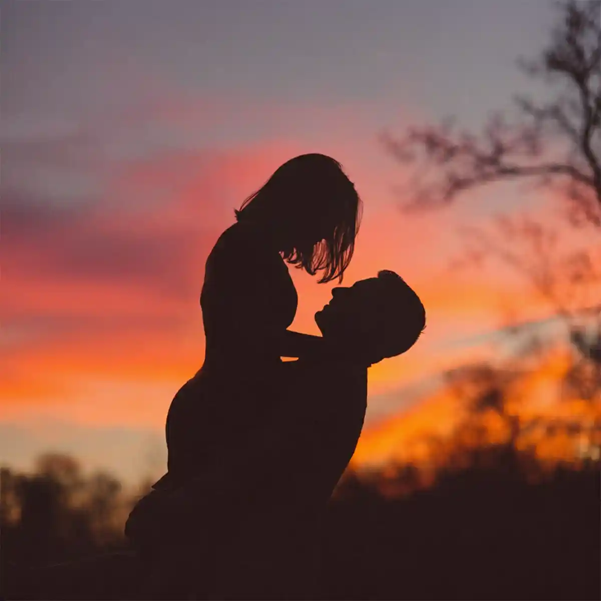 Silhouette di una coppia abbracciata controluce davanti al cielo arancione del tramonto