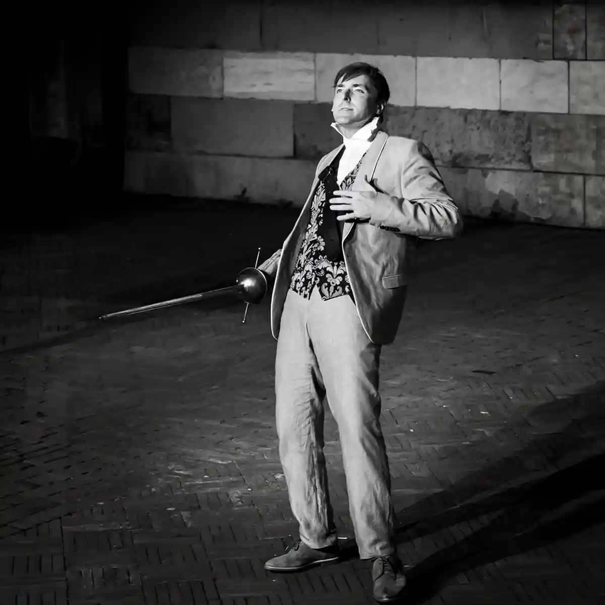 Attore in costume con spada durante uno spettacolo teatrale all'aperto, ritratto in bianco e nero