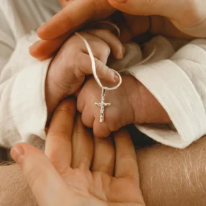 Le mani dei genitori racchiudono la manina del neonato con il crocifisso d'argento, battesimo a Genova