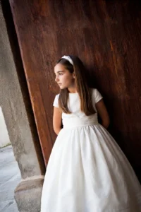 Ritratto di bambina in abito bianco appoggiata a un antico portone di legno nel giorno della prima comunione a Genova