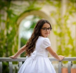 Ritratto di bambina in abito bianco appoggiata a una ringhiera nel giorno della prima comunione a Genova